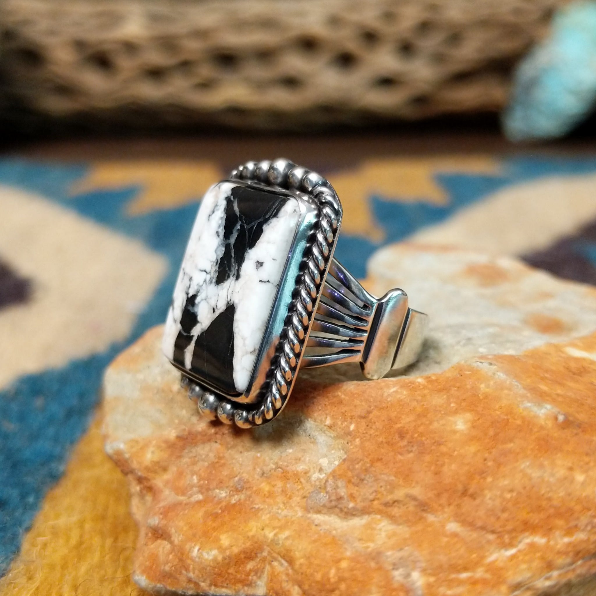 Handcrafted sterling silver White Buffalo ring by Alfred Martinez, featuring a rectangular White Buffalo gemstone with a twisted rope border and silver bead accents; side view.