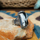 Handcrafted sterling silver White Buffalo ring by Alfred Martinez, featuring a rectangular White Buffalo gemstone with a twisted rope border and silver bead accents; side view.