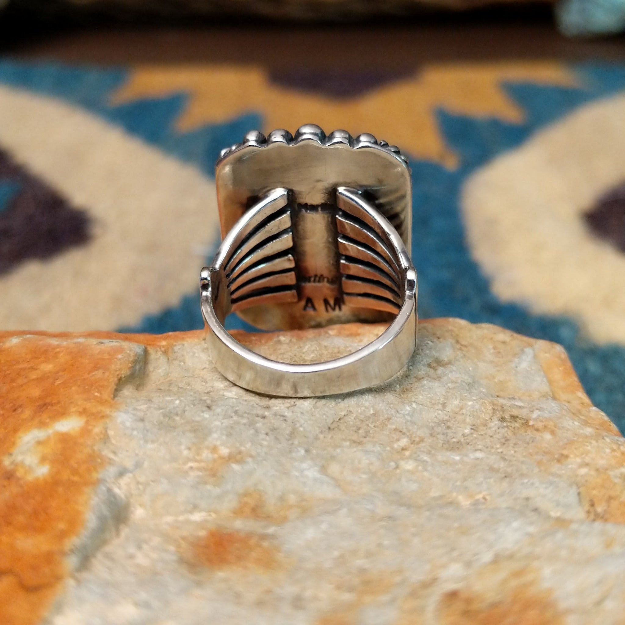 Handcrafted sterling silver White Buffalo ring by Alfred Martinez, featuring a rectangular White Buffalo gemstone with a twisted rope border and silver bead accents; underside view.