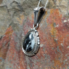 Handcrafted sterling silver White Buffalo teardrop pendant by Samuel Yellowhair, featuring a natural black-and-white White Buffalo gemstone in a twisted rope bezel; side view.