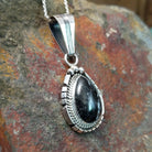 Handcrafted sterling silver White Buffalo teardrop pendant by Samuel Yellowhair, featuring a natural black-and-white White Buffalo gemstone in a twisted rope bezel; side view.