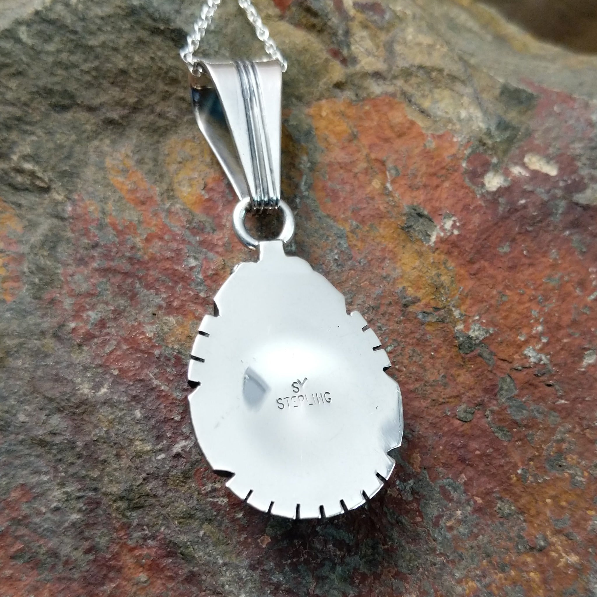 Handcrafted sterling silver White Buffalo teardrop pendant by Samuel Yellowhair, featuring a natural black-and-white White Buffalo gemstone in a twisted rope bezel; artisan and Sterling Silver stamp.