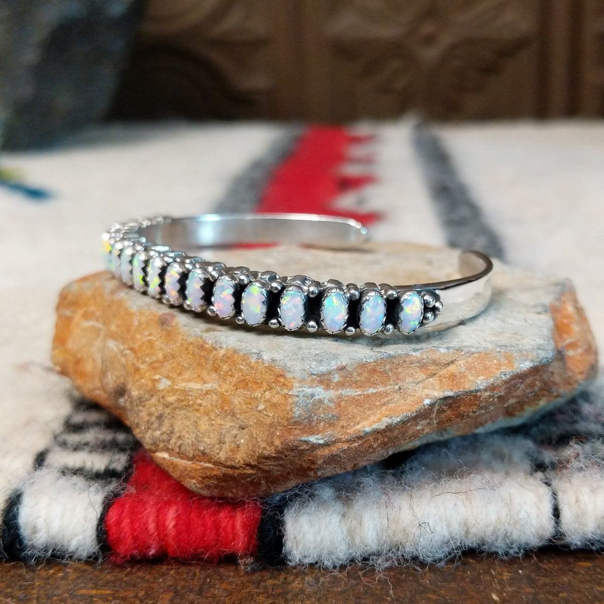 Silver cuff by Raymond Coriz featuring a single row of oval white manmade opals with colorful flashes of pink, green, yellow, and blue; side view.