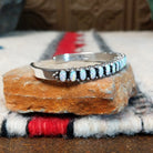 Silver cuff by Raymond Coriz featuring a single row of oval white manmade opals with colorful flashes of pink, green, yellow, and blue; side view.