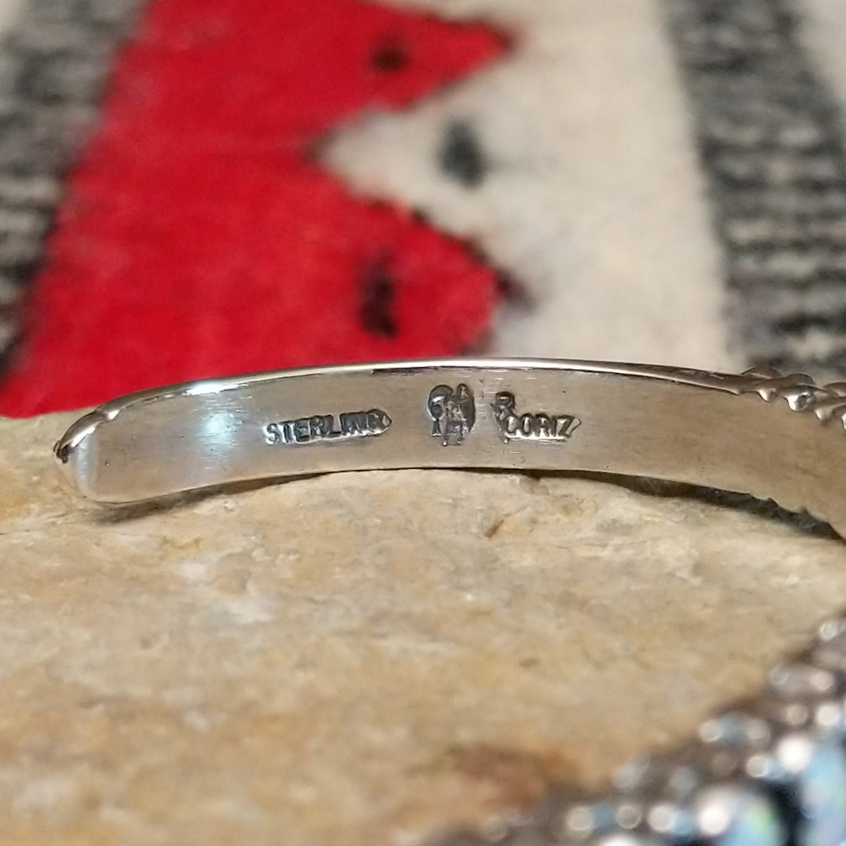 Silver cuff by Raymond Coriz featuring a single row of oval white manmade opals with colorful flashes of pink, green, yellow, and blue; artisan and Sterling Silver stamp.