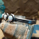 Sterling silver cuff bracelet with white, manmade opal set in a trio of round bezels, framed by showbox design and geometric setting.