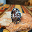 Front view of a Terry Wood sterling silver ring featuring an elongated oval Wild Horse stone with creamy white and reddish-brown marbling, framed by an asymmetrical silver border with stamped accents and rounded details.