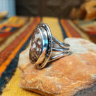 Side view of a Wild Horse stone ring featuring a raised oval bezel setting, decorative stamped silver border, and polished triple split-shank band.