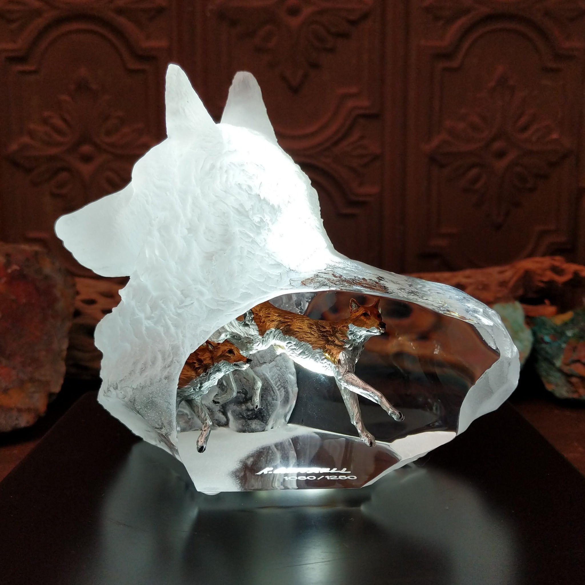 A frosted Lucite sculpture shaped like a wolf's head with a hand-painted wolf running inside the clear crystal interior, creating the illusion of movement; lower light display.