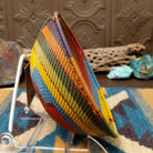 Handwoven wire art bowl by Bridge for Africa featuring a spiral pattern in recycled wire with olive green, mustard yellow, dusty blue, rust, terracotta, brown, and charcoal tones, perfect for home décor or wall display; side view.