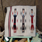 Yei Navajo rug by Milicent Platero featuring three traditional Yei figures on a natural gray background with geometric accents and a striped side border.