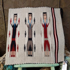 Yei Navajo rug by Milicent Platero featuring three traditional Yei figures on a natural gray background with geometric accents and a striped side border.