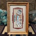 Framed Navajo sand painting of a side-facing Yei figure with turquoise accents and feather details. 