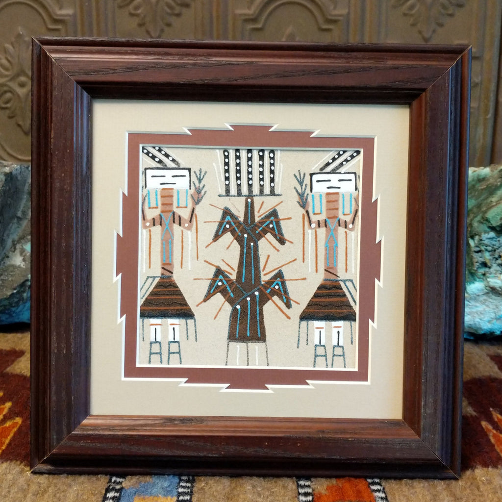 Sand painting of Yei and tree of life set within a dark wooden frame.