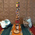 This distinctive Yellowface Shalako Kachina by John Taylor features a tall, slender wooden carving with a yellow face, intricate black geometric patterns, colorful red and turquoise blue accents, and a round wooden display base.