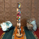 This distinctive Yellowface Shalako Kachina by John Taylor features a tall, slender wooden carving with a yellow face, intricate black geometric patterns, colorful red and turquoise blue accents, and a round wooden display base.