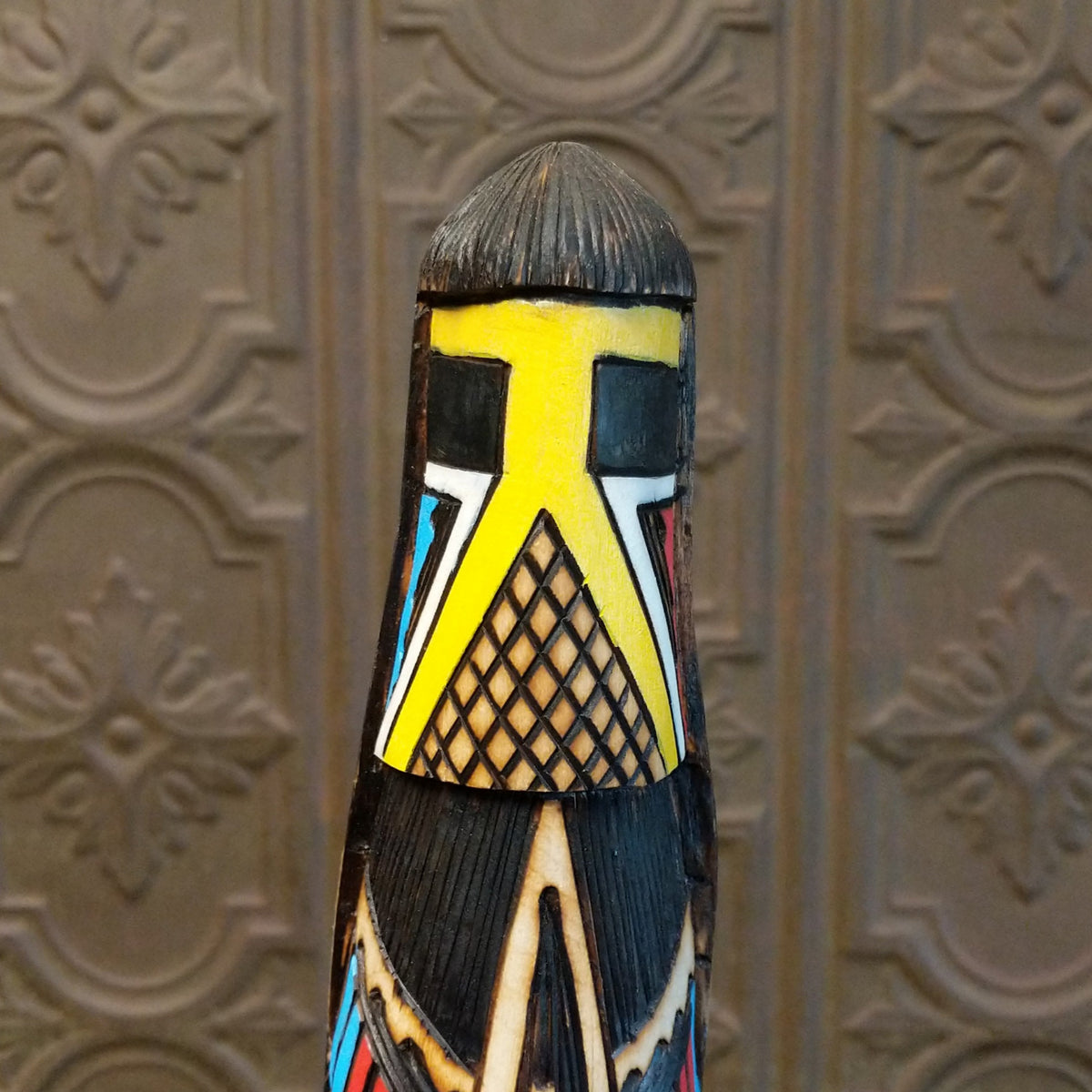 This distinctive Yellowface Shalako Kachina by John Taylor features a tall, slender wooden carving with a yellow face, intricate black geometric patterns, colorful red and turquoise blue accents, and a round wooden display base.