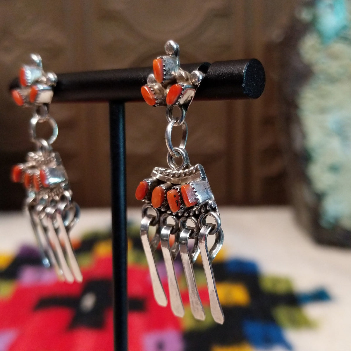 Zuni Coral Earrings featuring red-orange coral stones in detailed silver settings with clustered accents and multiple long dangling silver elements; side view.