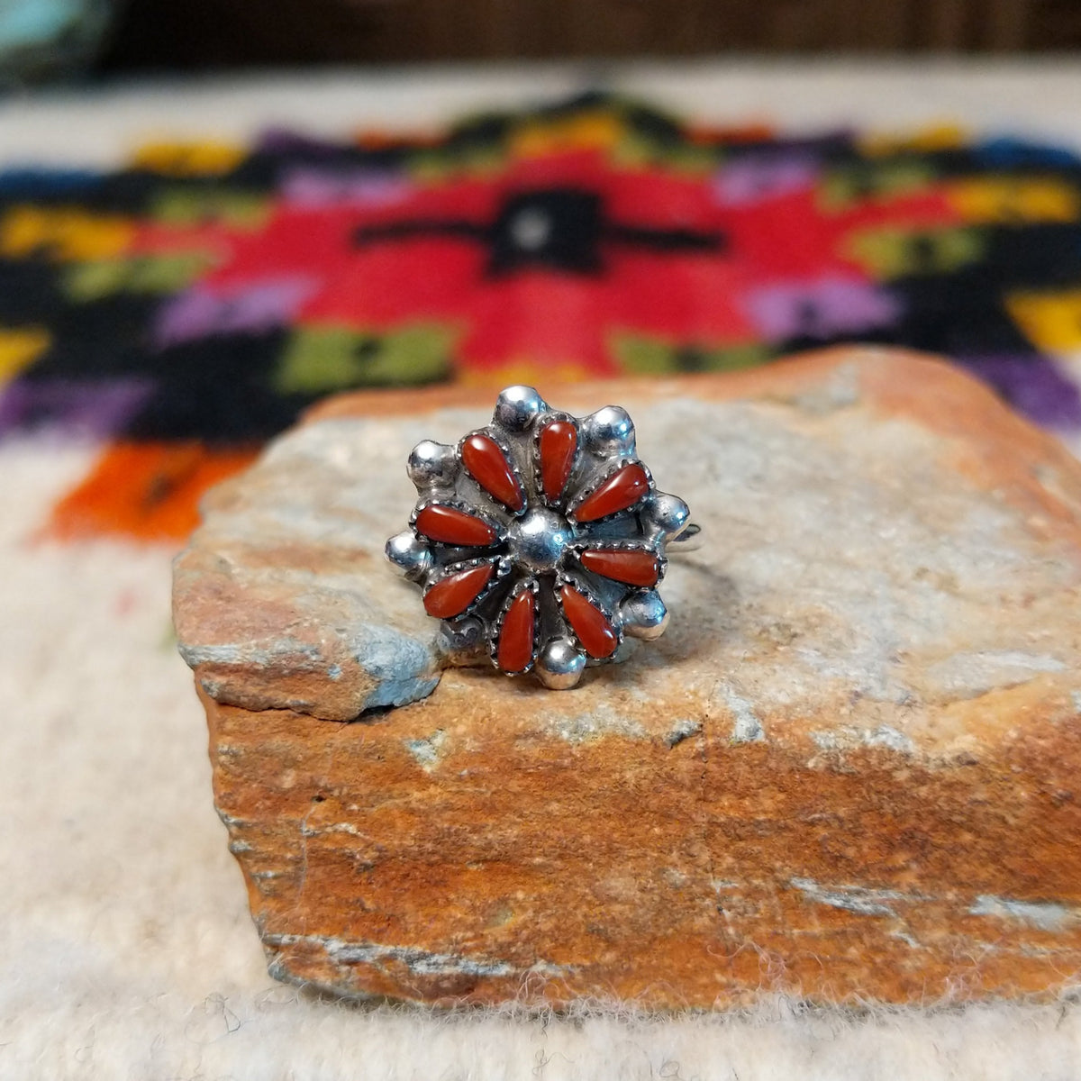 This vibrant Zuni Coral Flower Ring features teardrop-shaped red coral stones arranged as flower petals around a raised silver center, accented with rounded silver details.