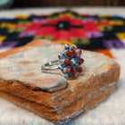 This vibrant Zuni Coral Flower Ring features teardrop-shaped red coral stones arranged as flower petals around a raised silver center, accented with rounded silver details; side view.