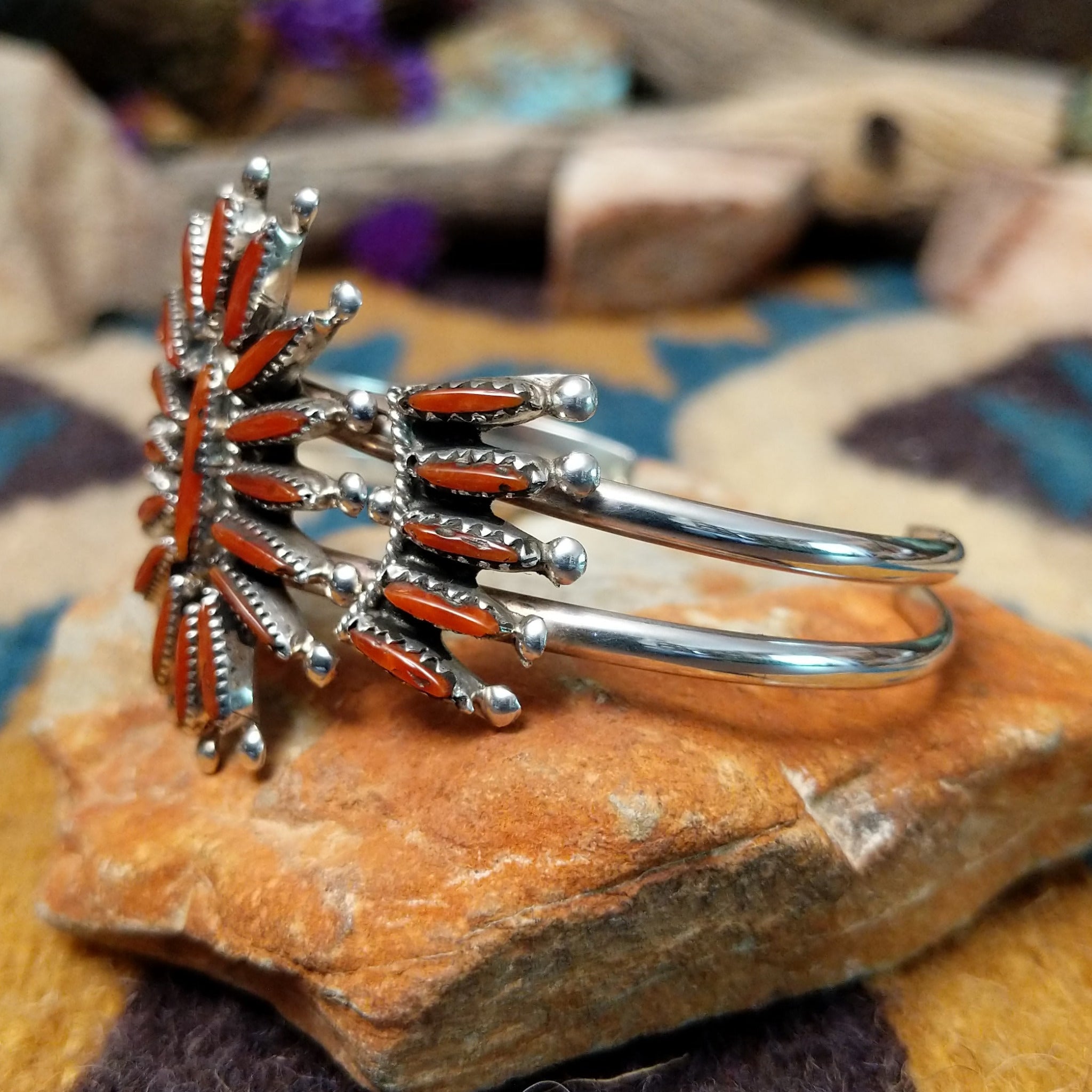 Handcrafted Zuni sterling silver cuff by G.E. featuring coral needlepoint stones in a traditional concho design with silver bead accents and a triple-shank cuff; side view.
