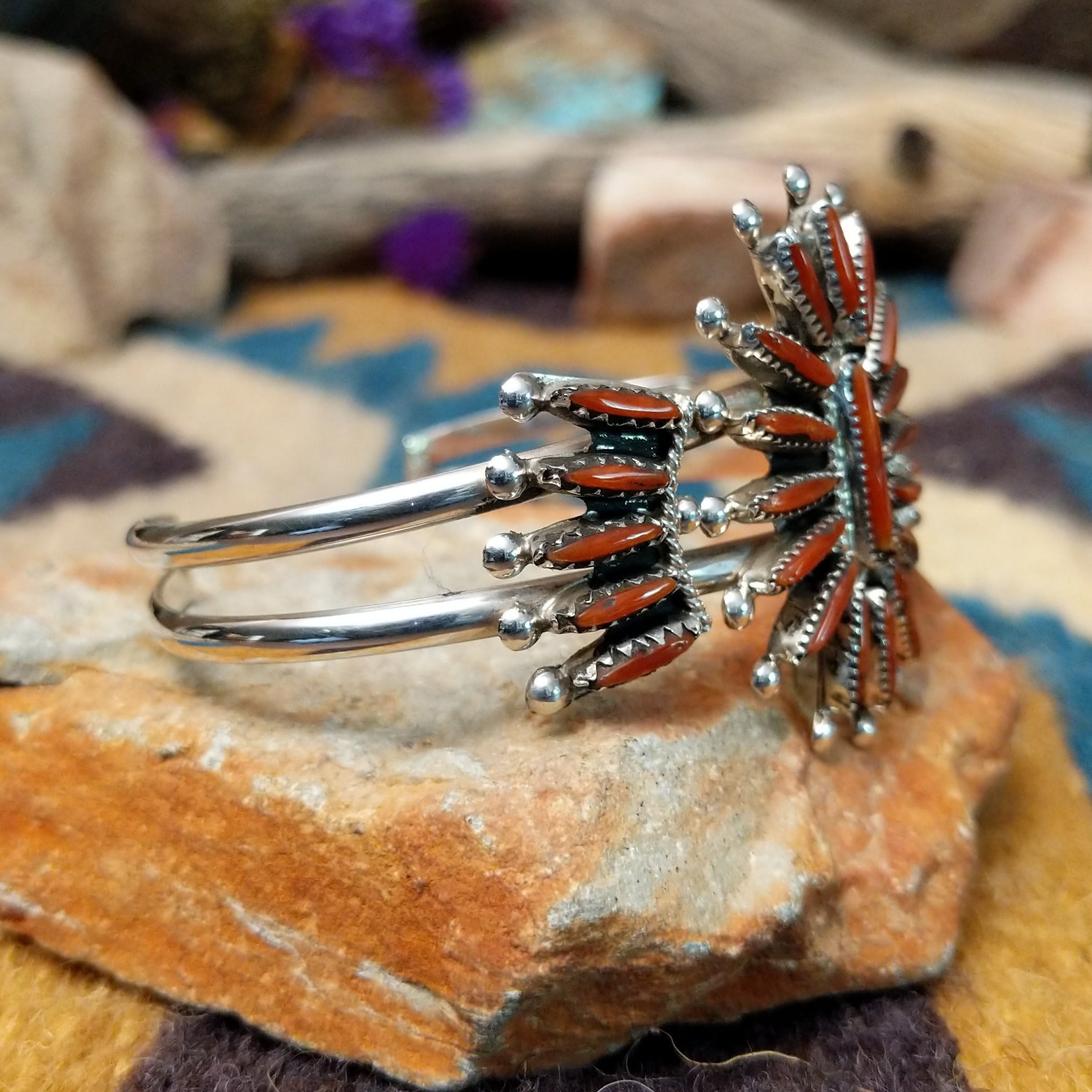 Handcrafted Zuni sterling silver cuff by G.E. featuring coral needlepoint stones in a traditional concho design with silver bead accents and a triple-shank cuff; side view.