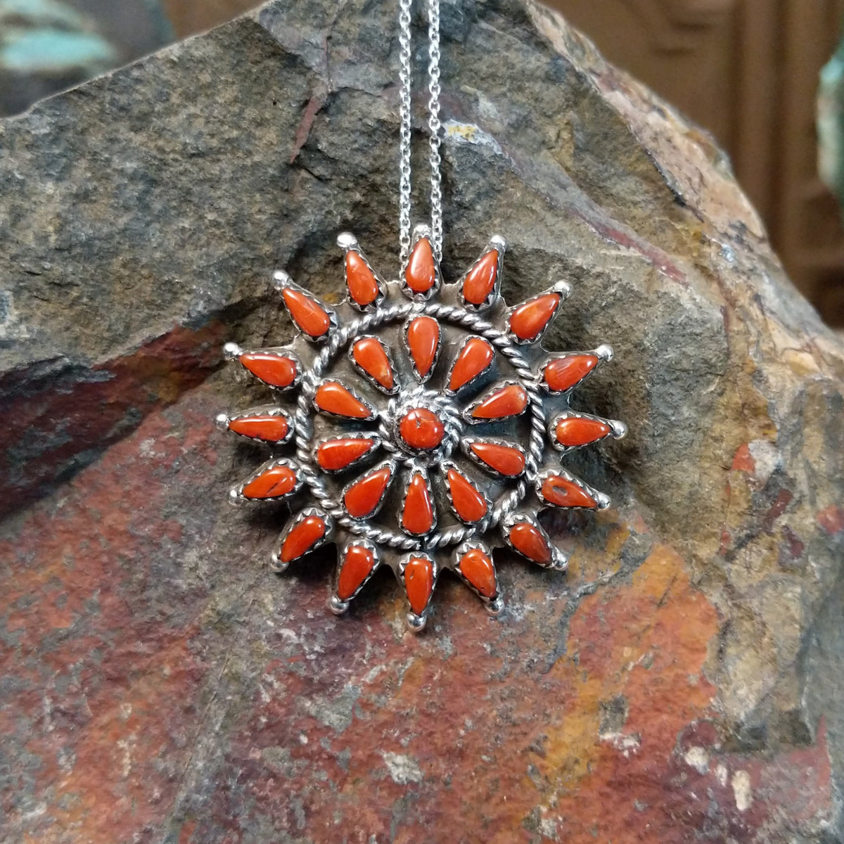 Zuni coral pendant and pin featuring red-orange teardrop-shaped coral stones arranged in a circular sunburst cluster with twisted silver detailing.