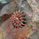 Zuni coral pendant and pin featuring red-orange teardrop-shaped coral stones arranged in a circular sunburst cluster with twisted silver detailing; side view.
