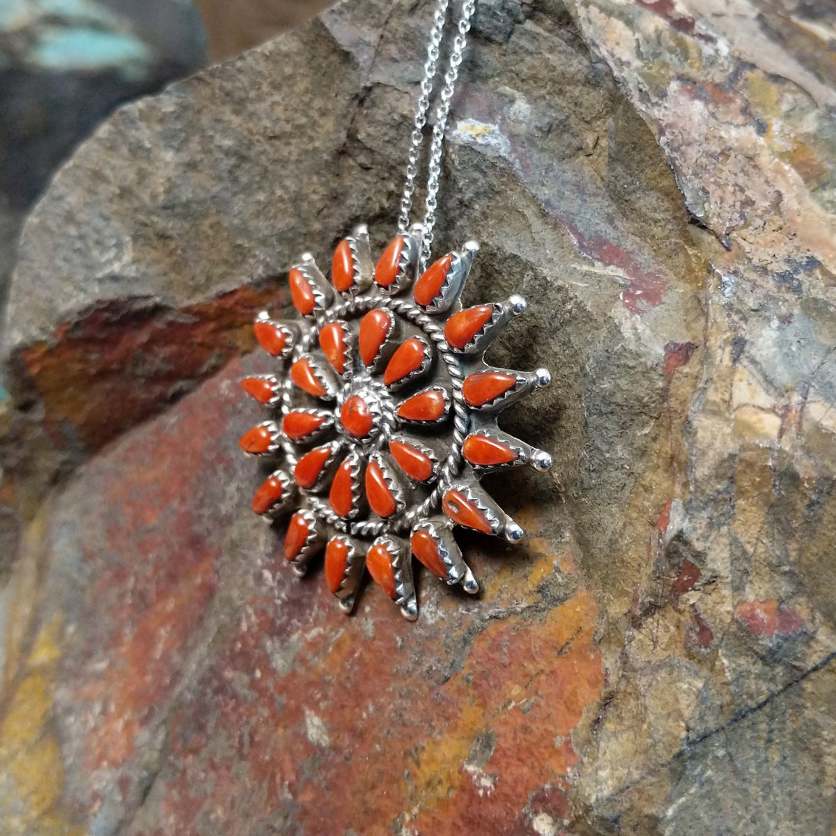 Zuni coral pendant and pin featuring red-orange teardrop-shaped coral stones arranged in a circular sunburst cluster with twisted silver detailing; side view.