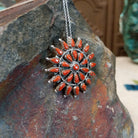 Zuni coral pendant and pin featuring red-orange teardrop-shaped coral stones arranged in a circular sunburst cluster with twisted silver detailing; side view.
