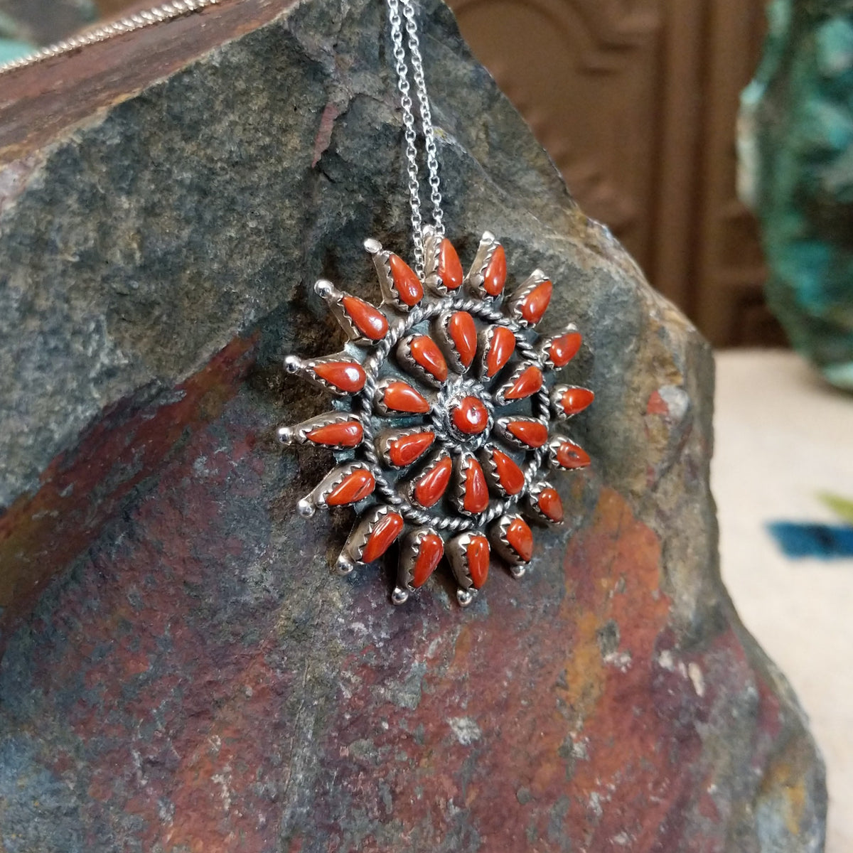 Zuni coral pendant and pin featuring red-orange teardrop-shaped coral stones arranged in a circular sunburst cluster with twisted silver detailing; side view.