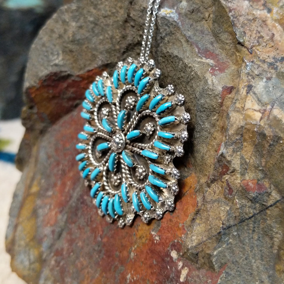 Zuni flowery needlepoint turquoise pendant and pin by Leekity featuring slender turquoise stones, twisted silver wire floral patterns, and decorative silver bead accents; side view.