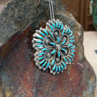 Zuni flowery needlepoint turquoise pendant and pin by Leekity featuring slender turquoise stones, twisted silver wire floral patterns, and decorative silver bead accents; side view.