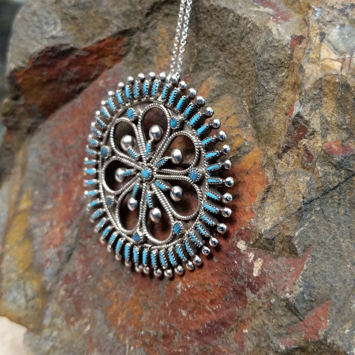 Zuni needlepoint turquoise pendant and pin by Vincent Johnson featuring slender turquoise stones arranged around a circular silver frame with intricate twisted-wire floral details and silver accents; side view.