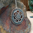 Zuni needlepoint turquoise pendant and pin by Vincent Johnson featuring slender turquoise stones arranged around a circular silver frame with intricate twisted-wire floral details and silver accents; side view.