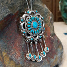 Zuni turquoise dangle pendant and pin by Lorraine Waatsa featuring a floral turquoise cluster, polished silver loops, twisted-wire detailing, and five turquoise-accented dangles; side view.