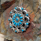 Zuni turquoise pendant and pin by Lorraine Waatsa featuring a floral cluster of turquoise stones surrounded by polished silver loops, twisted wire, and silver bead detailing; side view.