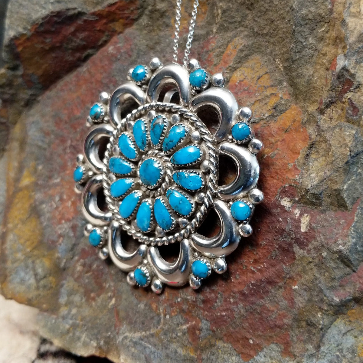 Zuni turquoise pendant and pin by Lorraine Waatsa featuring a floral cluster of turquoise stones surrounded by polished silver loops, twisted wire, and silver bead detailing; side view.