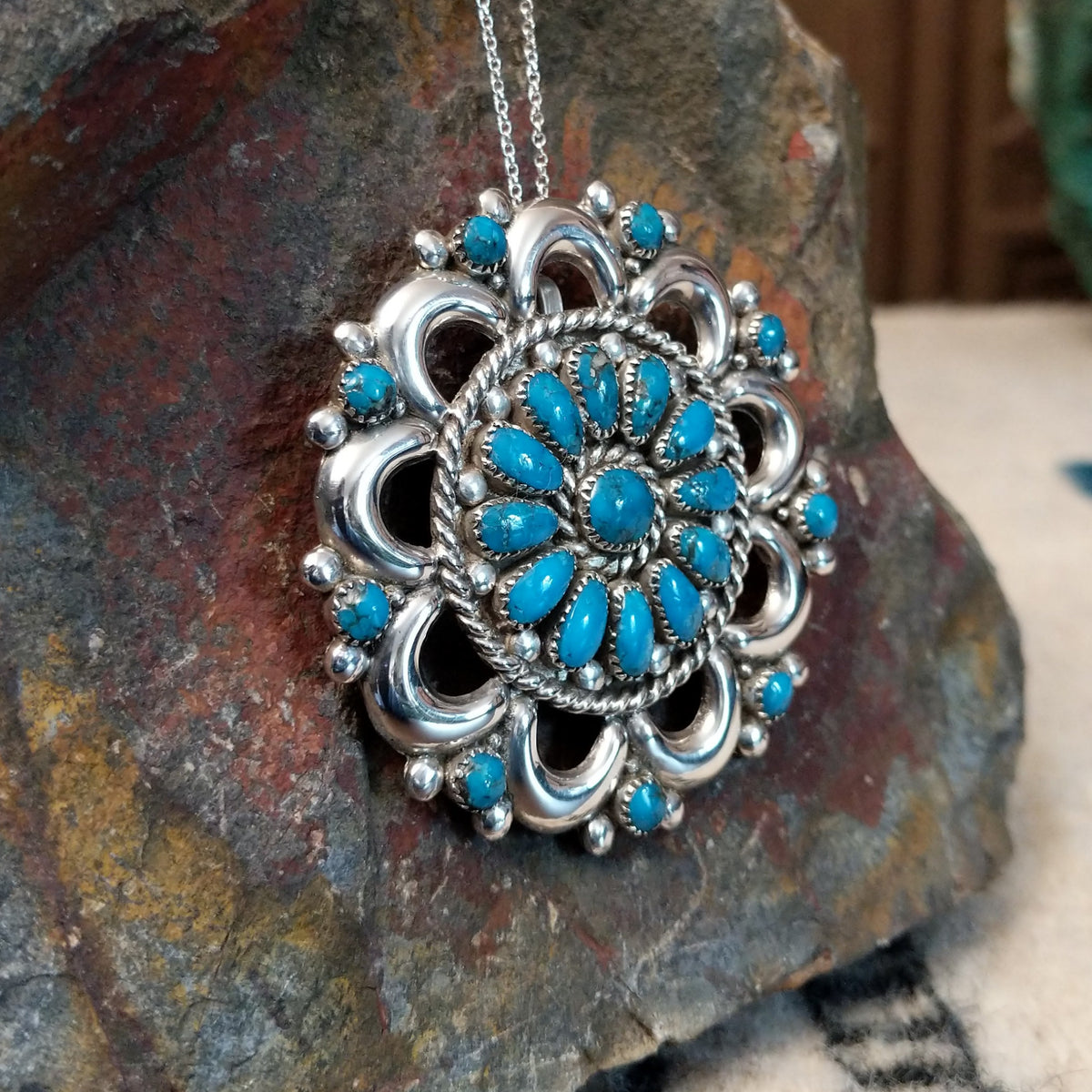Zuni turquoise pendant and pin by Lorraine Waatsa featuring a floral cluster of turquoise stones surrounded by polished silver loops, twisted wire, and silver bead detailing; side view.