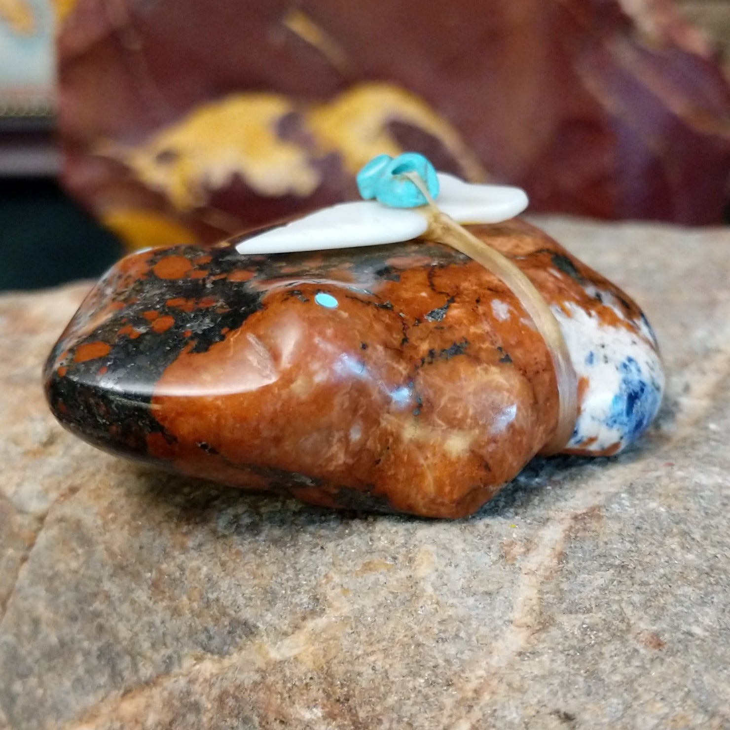 Brown and black matrix stone carved into a frog fetish with turquoise and mother of pearl tied to its' back.