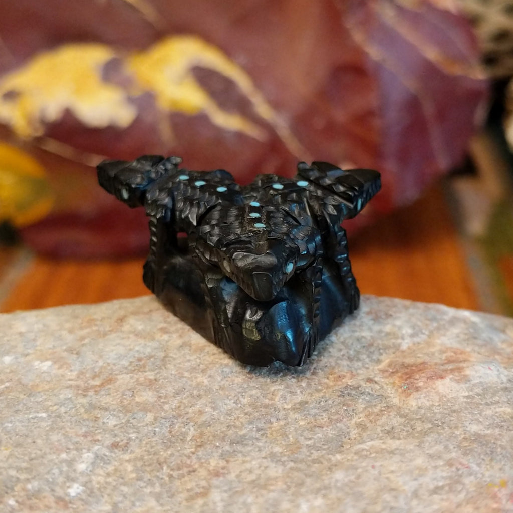 Three black onyx carved horned toad fetishes on a rock.