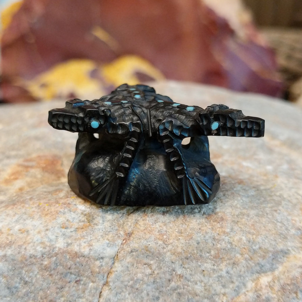 Three black onyx carved horned toad fetishes on a rock.