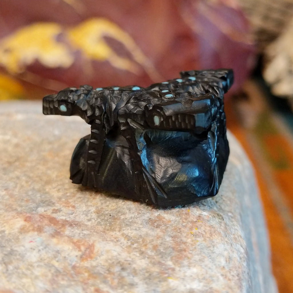 Three black onyx carved horned toad fetishes on a rock.