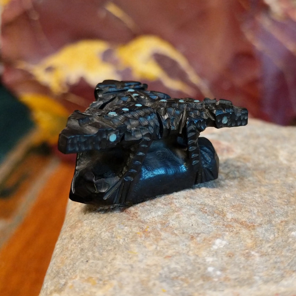Three black onyx carved horned toad fetishes on a rock.