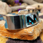 Handcrafted sterling silver Zuni cuff by Leander & Lisa Othole featuring a bold geometric channel inlay design with a polished sterling silver cuff and traditional Southwestern craftsmanship; side view.