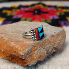 This colorful Zuni Inlay Ring features rectangular turquoise, black, and reddish-orange stone inlay in a geometric pattern, framed in silver with beaded accents along the sides; side view.
