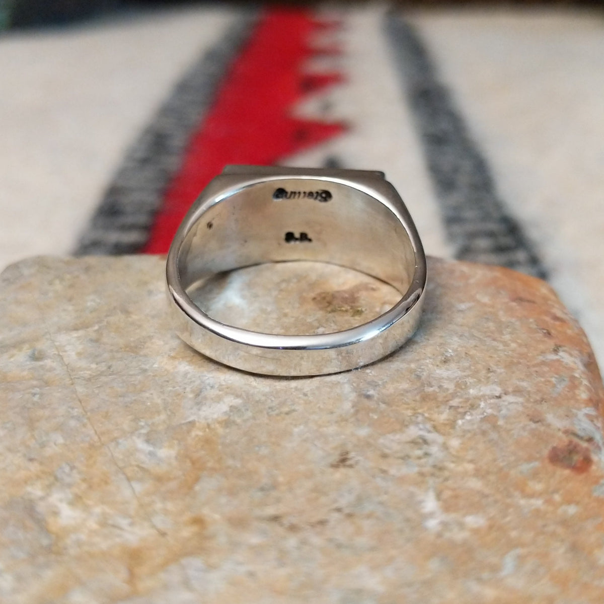 Zuni inlay ring by S.B. featuring a rectangular geometric design in turquoise, black onyx, coral, and mother of pearl inlay set in a polished silver band; underside view.