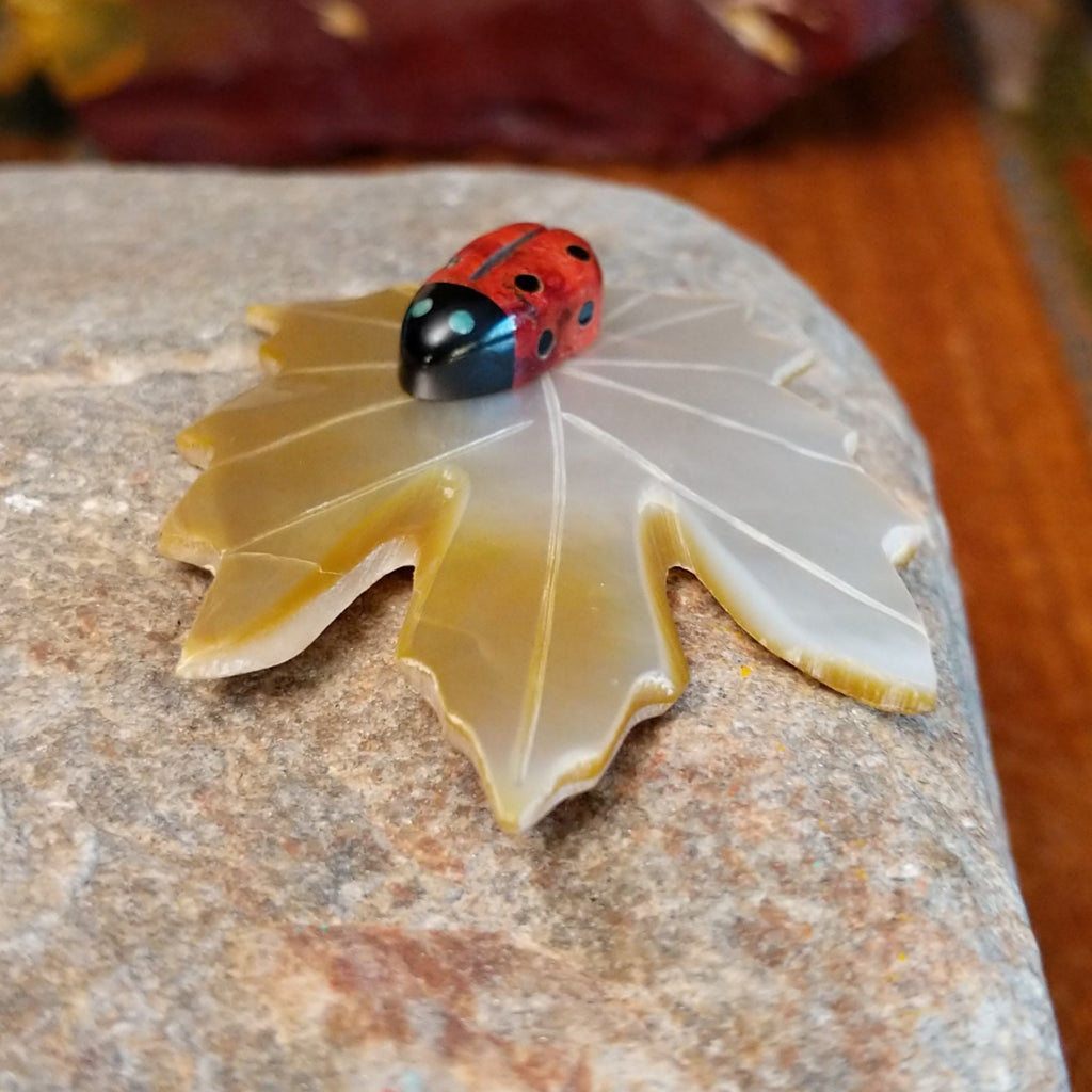 Apple coral ladybug carving with black onyx on a mother of pearl carved leaf.
