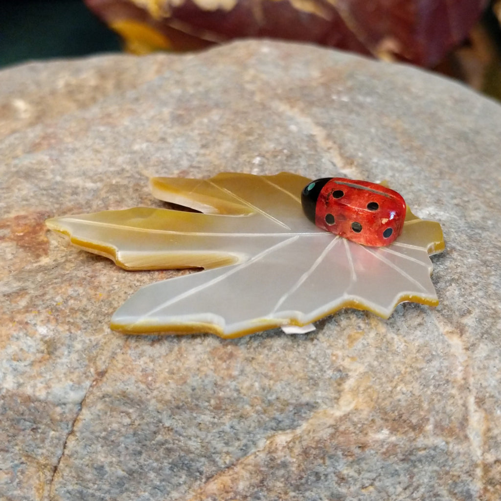 Apple coral ladybug carving with black onyx on a mother of pearl carved leaf.
