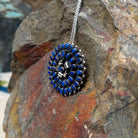 Zuni lapis cluster pendant and pin by Lorraine Waatsa featuring deep blue lapis stones arranged in concentric circles with twisted and sculptural silver detailing; side view.